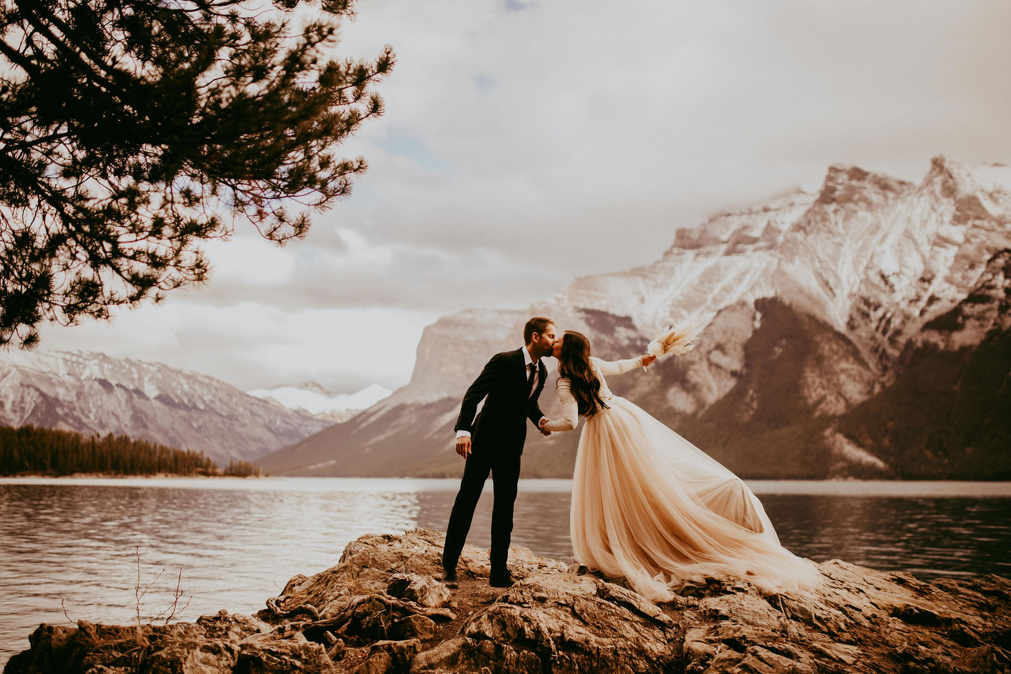 A bride and groom kiss in front of a glacier lake, without the mountains of Banff, Canada behind them.